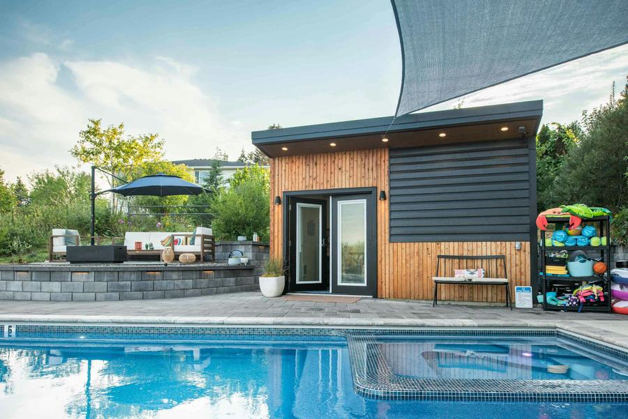 The cedar and black pool house with glass doors, a rack of pool toys and the patio lounge