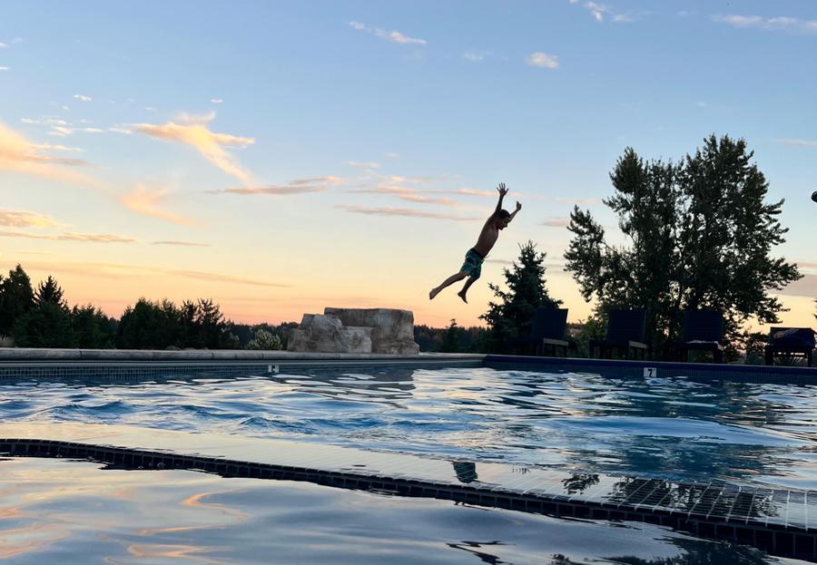 A swimmer mid-jump over the pool at sunset